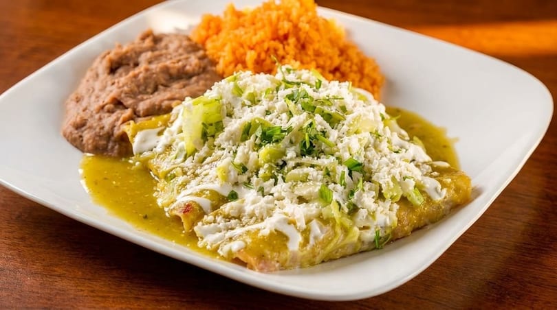Green enchiladas topped with cheese and lettuce, served with refried beans and orange rice.